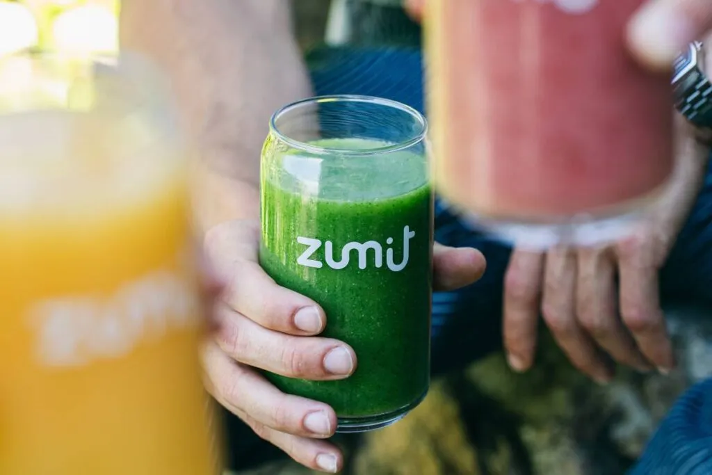 Smoothie Zumit Green Power con pepino, col rizada, piña y espinaca sujetado por una mano