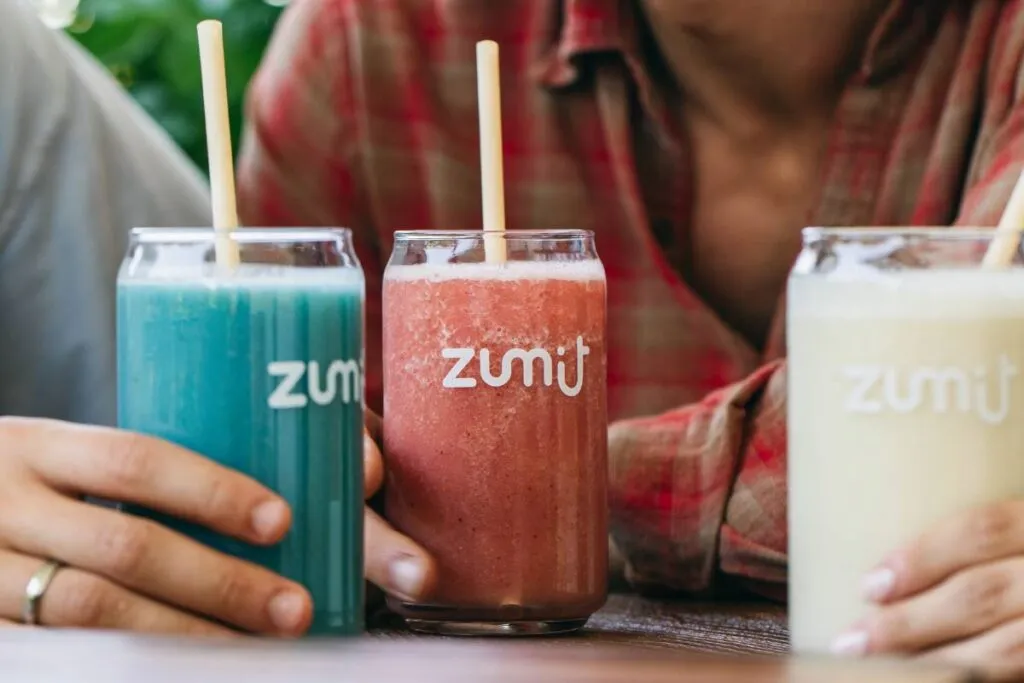 Smoothies Zumit Blue Lightning, Berries Paradise y Colada Jungle sobre una mesa de madera en manos de personas