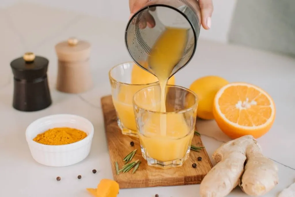 zumo de naranja sirviéndose en un vaso sobre una tabla de madera en una mesa con naranjas 