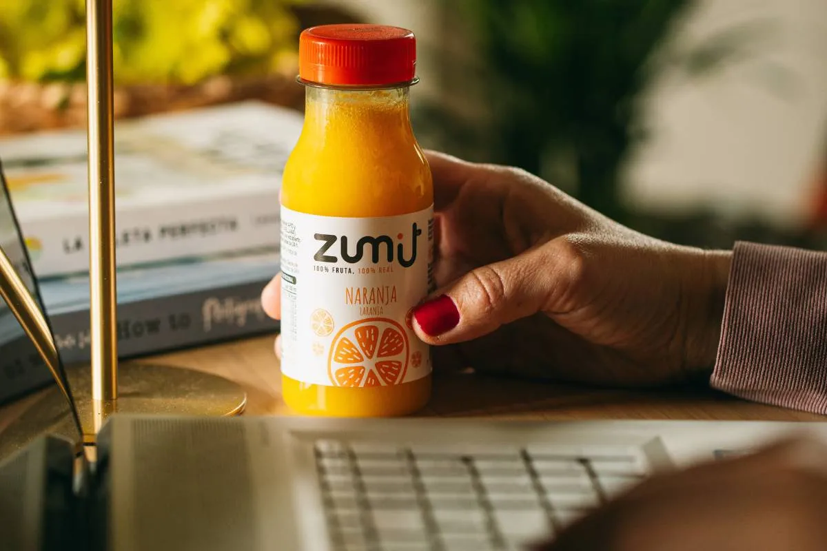 Zumo cold pressed Naranja de Zumit en una mesa de escritorio al lado de un ordenador portátil